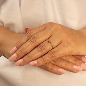 Peut inclure: Une d&eacute;licate bague en or avec une seule pierre pr&eacute;cieuse rouge. La bague est port&eacute;e &agrave; l'annulaire d'une main avec un vernis &agrave; ongles rose clair.