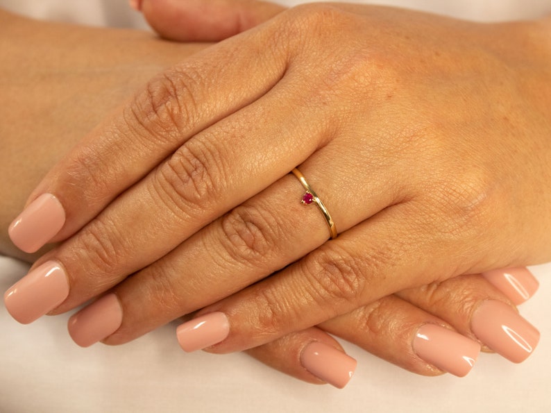 Peut inclure: Une d&eacute;licate bague en or avec une petite pierre pr&eacute;cieuse rouge vif sertie au centre.
