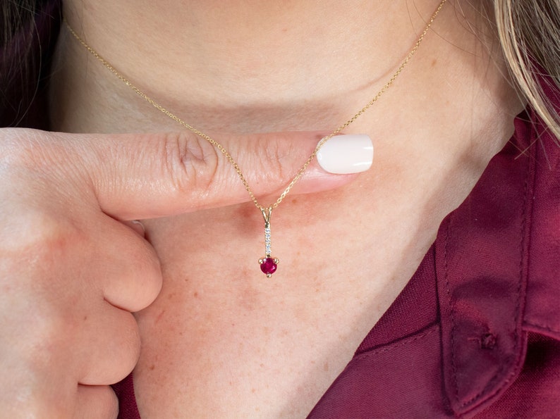 Puede incluir: Un collar de cadena de oro con un colgante que presenta una piedra roja rodeada de piedras blancas m&aacute;s peque&ntilde;as.