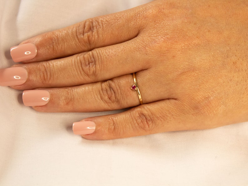 Peut inclure: Une d&eacute;licate bague en or avec une petite pierre pr&eacute;cieuse rouge en forme de c&oelig;ur.