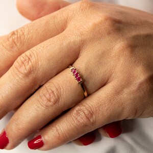 Pu&ograve; includere: Un anello d'oro con tre pietre preziose rosse disposte in fila.