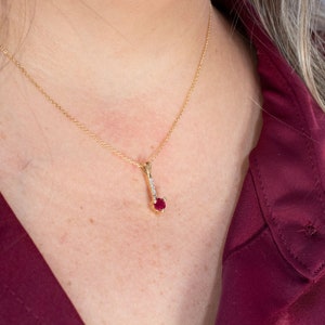 Puede incluir: Un collar de cadena de oro con un colgante que presenta una sola piedra roja rodeada de piedras transparentes m&aacute;s peque&ntilde;as.