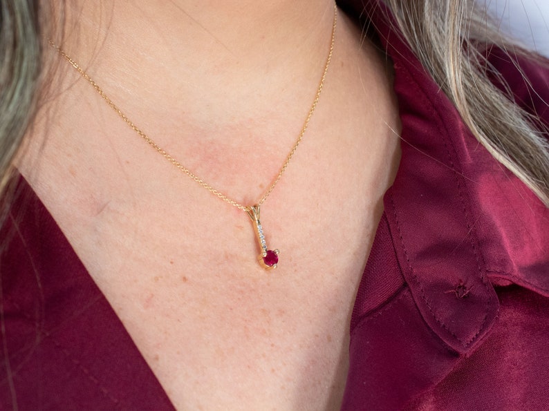 Puede incluir: Un collar de cadena de oro con un colgante que presenta una sola piedra roja rodeada de piedras transparentes m&aacute;s peque&ntilde;as.