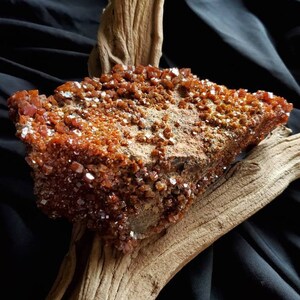 May include: A large, rough, orange-brown rock covered in small, sparkling crystals. The rock is resting on a piece of driftwood.