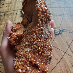 May include: A large, rough, orange-brown rock formation covered in small, sparkly, orange crystals. The crystals are clustered together and have a cubic shape.