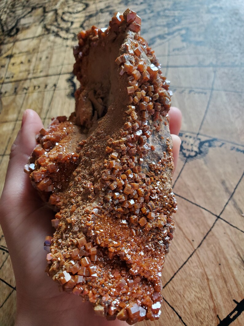 May include: A large, rough, orange-brown rock formation covered in small, sparkly, orange crystals. The crystals are clustered together and have a cubic shape.