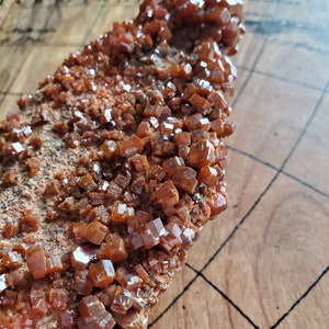 May include: A close-up of a rough, brown rock covered in small, shiny, orange crystals. The crystals are clustered together and have a cubic shape.