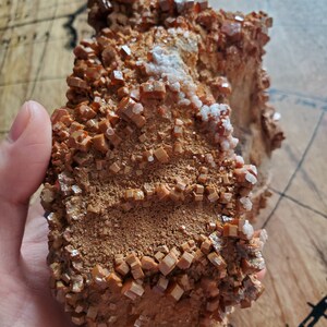 May include: A cluster of orange-brown crystals with a rough, textured surface. The crystals are arranged in a layered pattern, creating a unique and interesting visual.