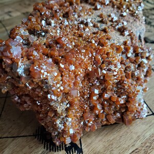 May include: A large, rough, orange-brown rock covered in small, shiny, orange crystals. The crystals are clustered together and have a cubic shape.