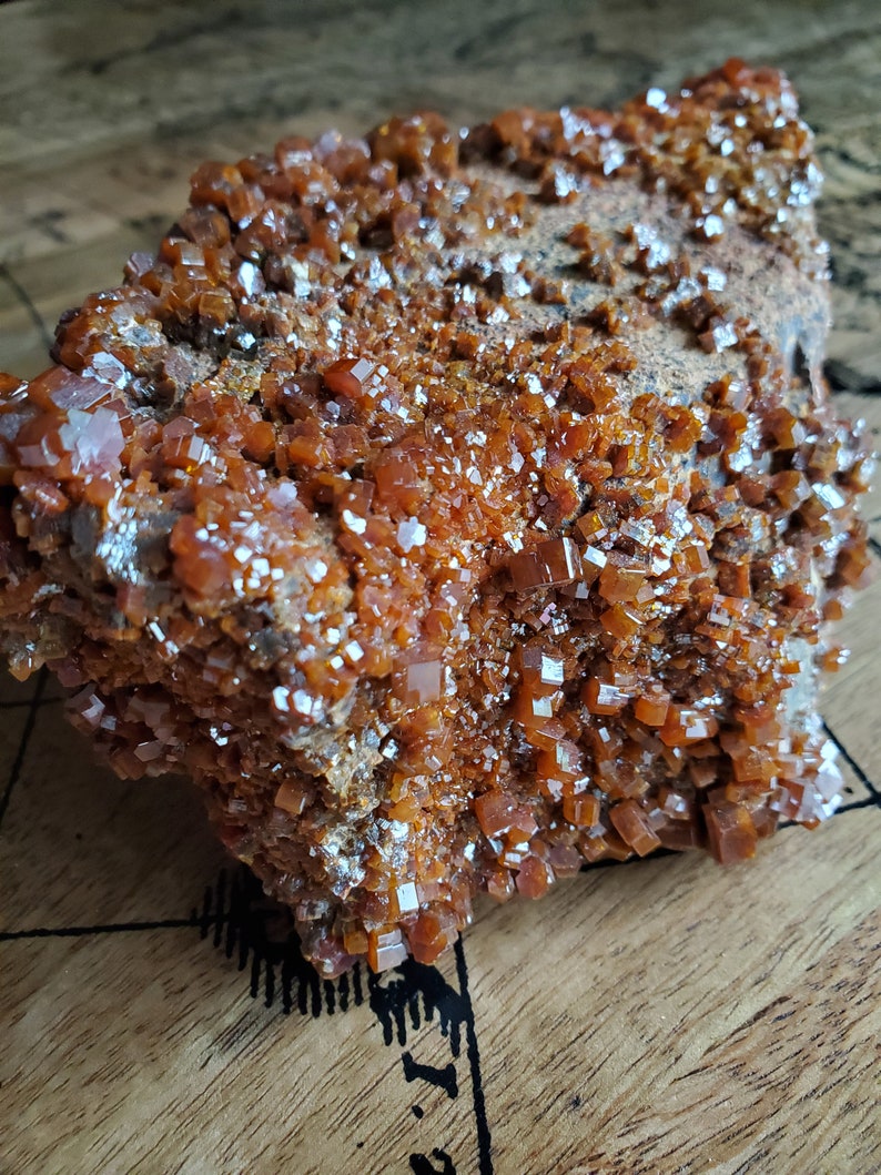 May include: A large, rough, orange-brown rock covered in small, shiny, orange crystals. The crystals are clustered together and have a cubic shape.