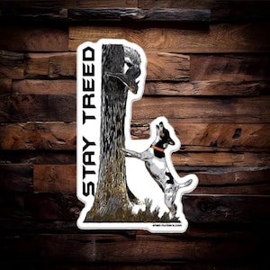 May include: A black and white dog with an orange collar is jumping up at a tree trunk. A squirrel is climbing up the tree trunk. The text "STAY TREED" is written vertically on the left side of the tree trunk. The image is a sticker.