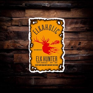 Peut inclure: Un autocollant rectangulaire avec un fond jaune vieilli et une bordure blanche. Il pr&eacute;sente le texte "ELKAHOLIC" au-dessus d'un graphique de wapiti rouge avec des flammes. En dessous, on lit "ELK HUNTER" et des phrases de chasse.