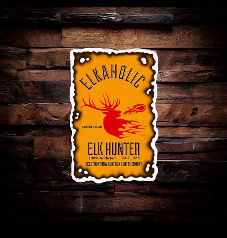 Peut inclure: Un autocollant rectangulaire avec un fond jaune vieilli et une bordure blanche. Il pr&eacute;sente le texte "ELKAHOLIC" au-dessus d'un graphique de wapiti rouge avec des flammes. En dessous, on lit "ELK HUNTER" et des phrases de chasse.