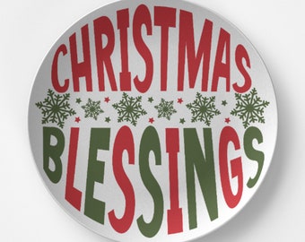 May include: A white ceramic plate with the words "CHRISTMAS BLESSINGS" in red and green. The plate features green snowflakes and red stars. A festive holiday decoration.
