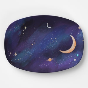 Könnte beinhalten: Ein ovaler Keramikteller in dunkelblau mit einem Sternenhimmel-Design. Der Teller zeigt eine Mondsichel, einen kleineren Mond, einen Planeten mit Ringen und goldene Sterne.