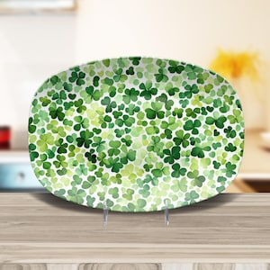May include: A white oval serving platter with a green shamrock pattern. The platter is on a wooden surface.