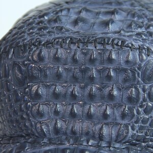 May include: A dark blue alligator skin hat with a stitched seam across the top.