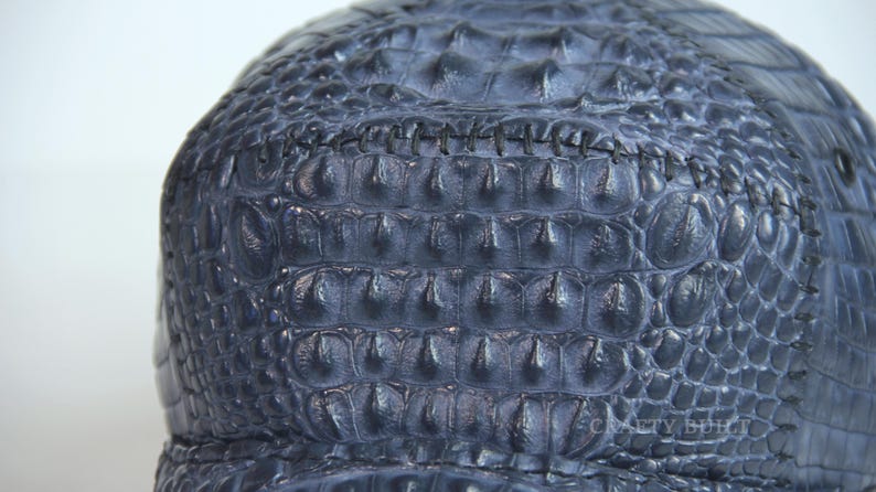 May include: A dark blue alligator skin hat with a stitched seam across the top.