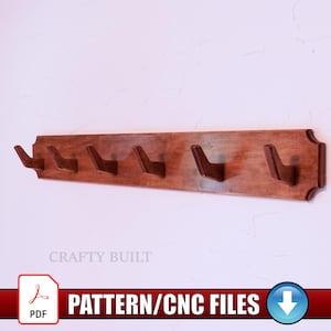 Puede incluir: Un perchero de madera con seis ganchos, montado en una pared blanca. El perchero está teñido de un color marrón cálido. El texto "PATTERN/CNC FILES" se muestra en una pancarta roja.