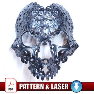 Puede incluir: Una máscara de calavera metálica detallada con un intrincado diseño de filigrana floral. La máscara es de color plata oscura y se muestra sobre un fondo blanco. El texto "PATTERN & LASER" es visible en la parte inferior.