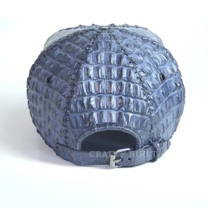 May include: A blue baseball cap made of crocodile leather. The cap has a strap with a buckle in the back.
