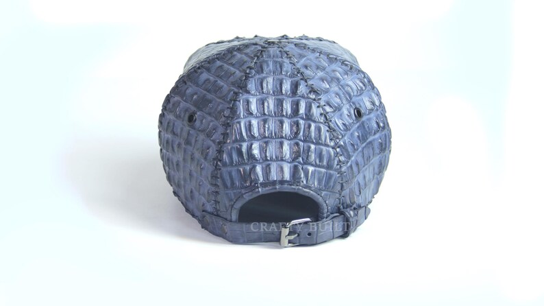 May include: A blue baseball cap made of crocodile leather. The cap has a strap with a buckle in the back.