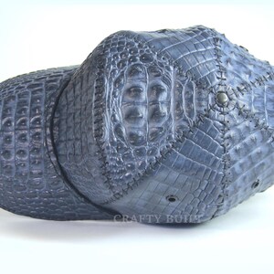 May include: A blue baseball cap made of crocodile leather. The cap has a stitched design and the text "CRAFTY BUILD" is visible on the front.