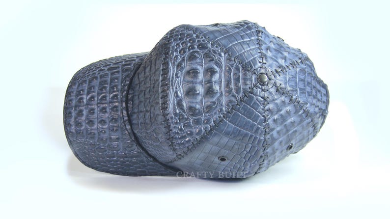 May include: A blue baseball cap made of crocodile leather. The cap has a stitched design and the text "CRAFTY BUILD" is visible on the front.