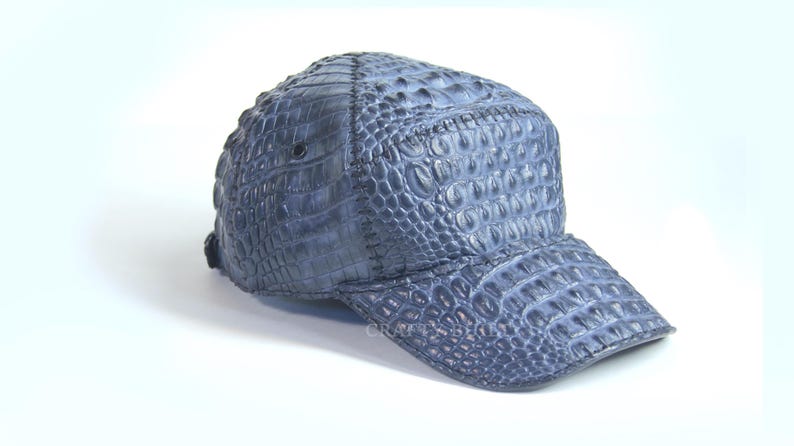 May include: A blue baseball cap made of crocodile leather. The cap has a curved brim and a textured surface.