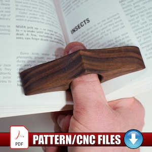 May include: A dark brown wooden thumb book holder with a V-shaped design, featuring a central circular hole for a thumb to rest while holding open the pages of an open book with text about birds and insects visible on the paper pages.
