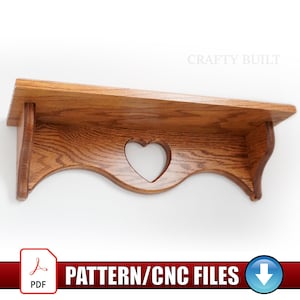 May include: A wooden shelf with a heart-shaped cutout and a scalloped edge. The shelf is made of light brown wood and is mounted on a white wall. The text "CRAFTY BUILT" is visible. The image also includes the text "PATTERN/CNC FILES".