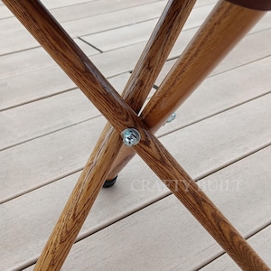 May include: Close-up of the wooden legs of a folding chair. The legs are made of natural wood and are connected with metal screws. The chair is sitting on a wooden deck.