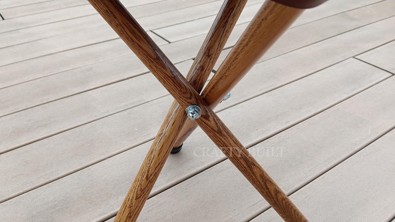 May include: Close-up of the wooden legs of a folding chair. The legs are made of natural wood and are connected with metal screws. The chair is sitting on a wooden deck.