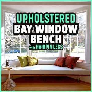 May include: Upholstered bay window bench with hairpin legs. The bench has a cream-colored cushion and is accented with green and red throw pillows. The bench is set in front of a large window with a view of trees and a car.