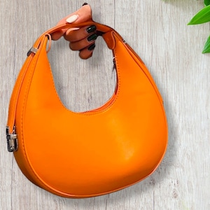 May include: A bright orange, crescent-shaped handbag with a silver clasp.