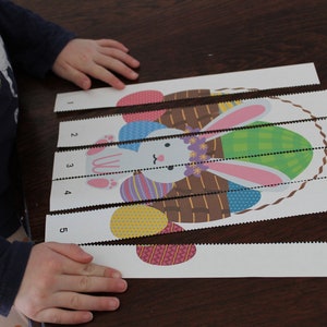 May include: A child's hands are shown assembling a five-piece puzzle of a bunny holding a basket of Easter eggs. The puzzle pieces are numbered 1 through 5.