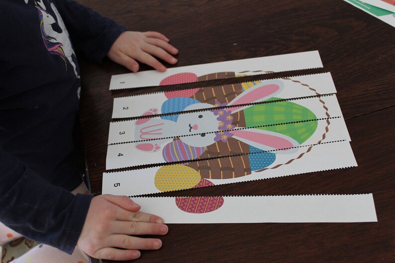 May include: A child's hands are shown assembling a five-piece puzzle of a bunny holding a basket of Easter eggs. The puzzle pieces are numbered 1 through 5.