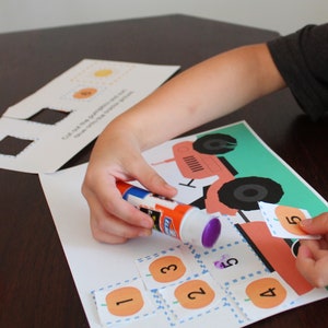 May include: A child uses glue to attach orange pumpkin-shaped number cards to a tractor-themed learning activity. The numbers 1, 2, 3, 4, and 5 are visible.