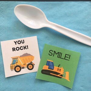 May include: Two construction-themed party favor tags. One tag is green with a yellow bulldozer and the text "SMILE!" The other tag is white with a yellow dump truck and the text "YOU ROCK!"