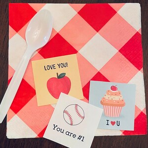 May include: Three small cards with different designs on a red and white checkered background. The first card has a red apple with a green stem and leaf and the text "LOVE YOU!" The second card has a baseball and the text "You are #1". The third card has a cupcake with a cherry on top and the text "I &hearts; U".