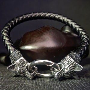 May include: A black leather bracelet with silver wolf head accents and a silver clasp.