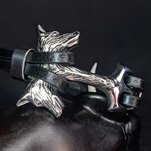 Op de afbeelding: Een zilveren armband met een wolfskop en zwarte leren banden. De wolfskop is gedetailleerd en heeft een textuur.