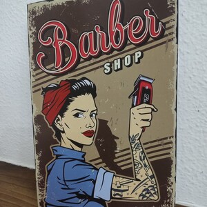 May include: A vintage-style poster featuring a woman holding an electric razor. The poster is brown with red, white and blue accents. The text on the poster reads "Barber Shop".