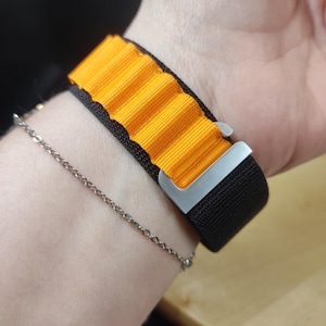 Könnte beinhalten: Ein schwarzes und orangefarbenes Armband mit einer silbernen Schnalle. Das Armband hat ein strukturiertes, geripptes Design.