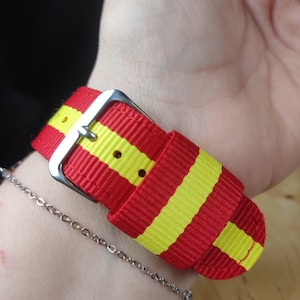 May include: A red and yellow striped watch band with a silver buckle.