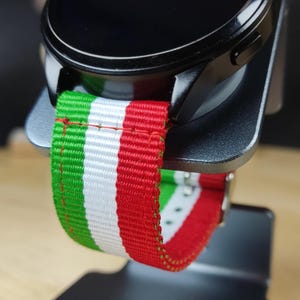 May include: A black smartwatch with a green, white, and red striped watch band. The watch is on a gray stand with the word "remarkable" printed on it.