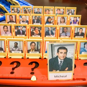 Puede incluir: Un tablero de juego amarillo y rojo con una cuadr&iacute;cula de peque&ntilde;os marcos de fotos. Cada marco contiene una foto de un personaje del programa de televisi&oacute;n "The Office". El tablero de juego tiene un signo de interrogaci&oacute;n en cada una de las cuatro esquinas. La fila inferior del tablero tiene los n&uacute;meros del 0 al 4. El tablero de juego est&aacute; titulado "Micheal".
