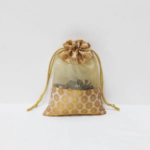 Puede incluir: Una pequeña bolsa de cordón de color dorado hecha de tela transparente con un patrón floral. La bolsa está llena de pequeños objetos oscuros.