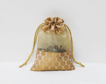 Könnte beinhalten: Eine kleine, goldene Kordeltasche aus durchsichtigem Stoff mit Blumenmuster. Die Tasche ist mit kleinen, dunklen Gegenständen gefüllt.