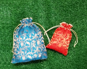 May include: Two drawstring pouches made of fabric with a metallic floral pattern. The larger pouch is blue with silver-toned floral designs, and the smaller pouch is red with gold-toned floral designs. Both feature cream-colored drawstrings.